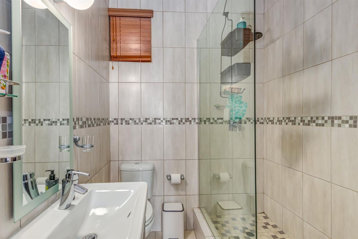 A compact, modern bathroom featuring a glass-enclosed shower, tiled walls with decorative mosaic accents, a wall-mounted vanity basin, and a toilet.