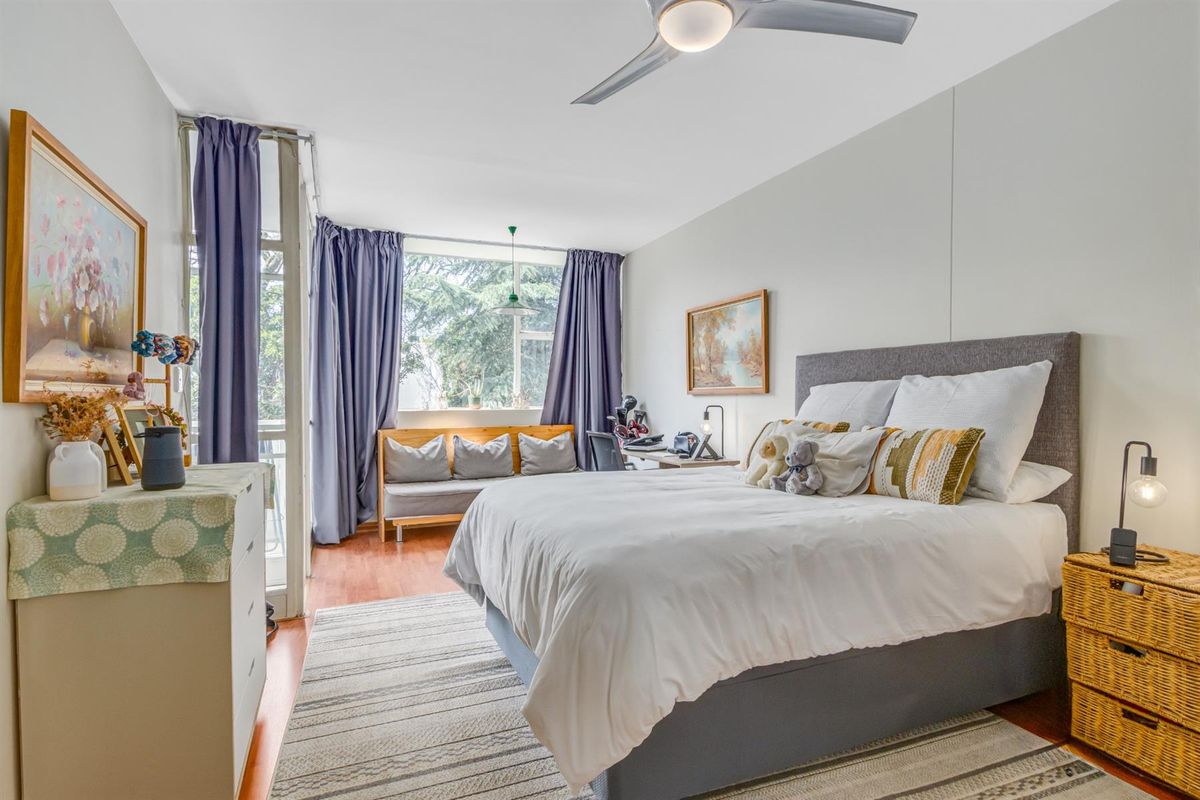 A well-lit bedroom featuring hardwood flooring, a ceiling fan, and large windows providing natural light and access to a balcony area.