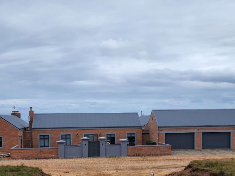 A well-maintained brick farmhouse featuring a triple garage, metal roofing, and a gated courtyard entrance set against a rural landscape.