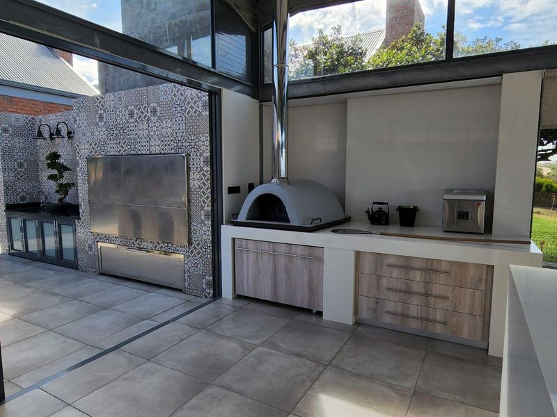Modern outdoor entertainment area featuring a built-in pizza oven, stainless steel braai, tiled splashbacks, and custom cabinetry with stone countertops.