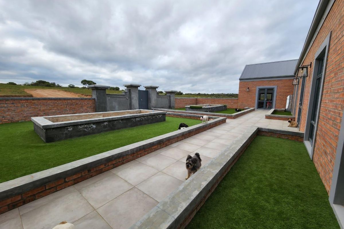 A well-maintained rear courtyard featuring paved walkways, raised brick and concrete planters, and artificial lawn areas, enclosed by a perimeter brick wall.