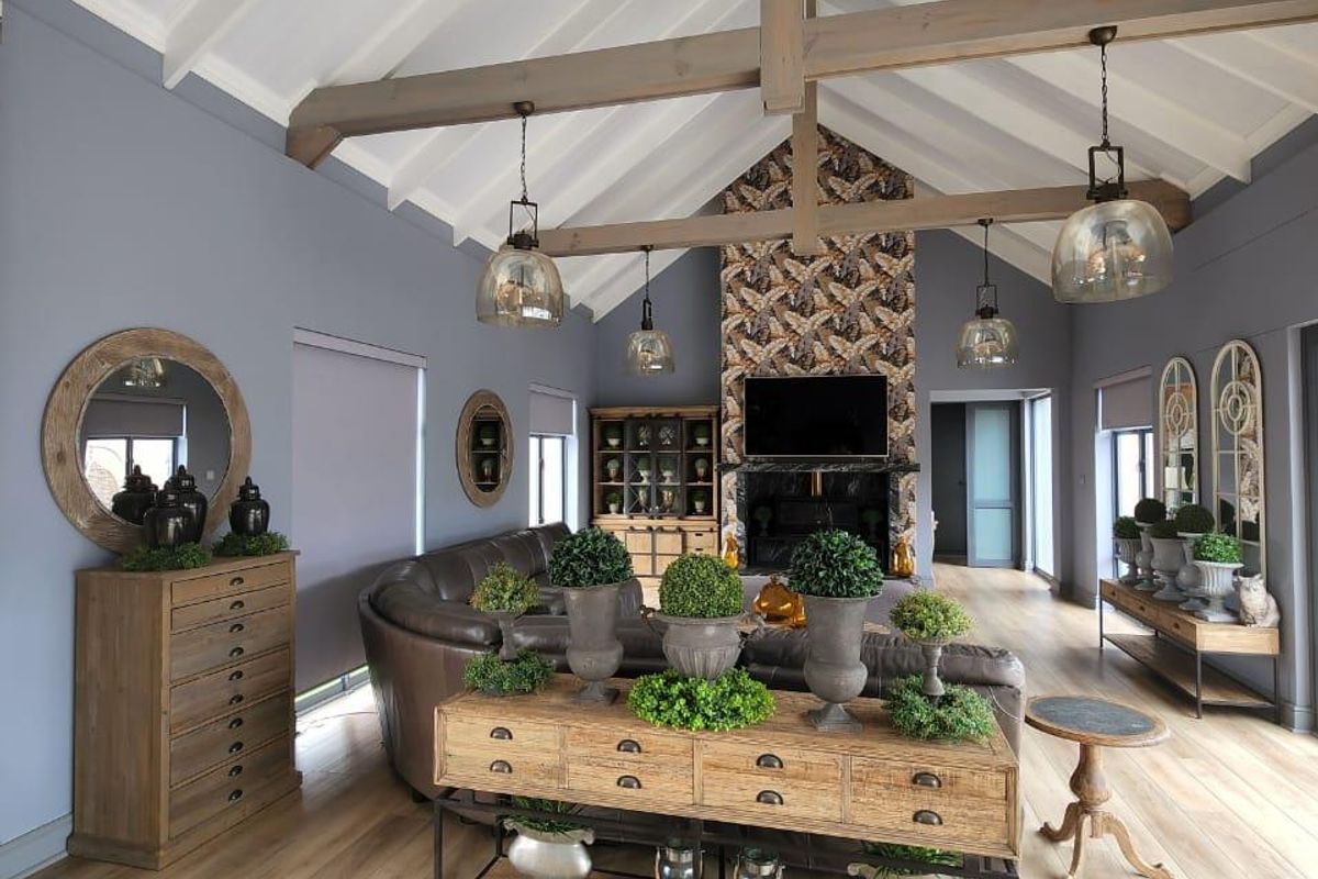 Spacious living room featuring a high vaulted ceiling with exposed timber beams, wood-look flooring, and a striking feature fireplace with patterned tiling.