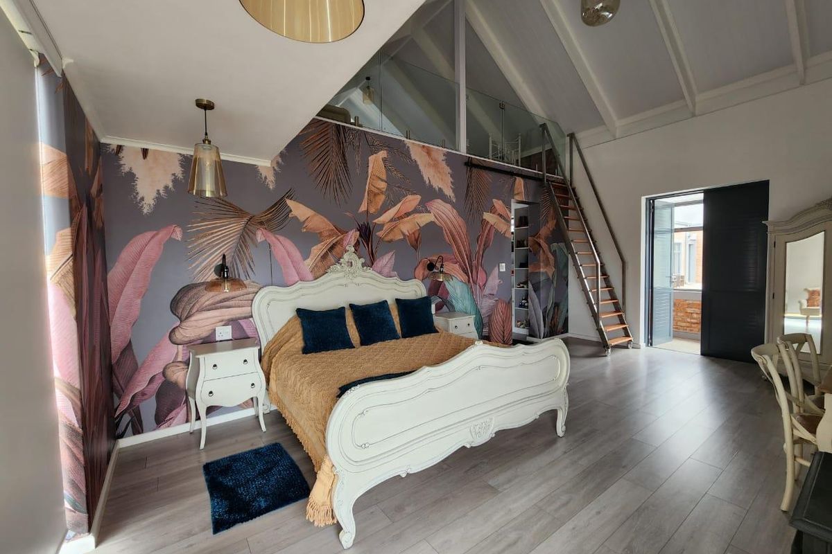 Spacious bedroom featuring a vaulted ceiling, laminate flooring, a mezzanine level with glass balustrade, and access to a private balcony.