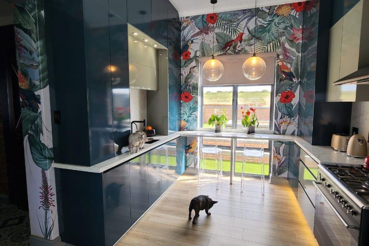 Modern kitchen featuring high-gloss dark cabinetry, integrated appliances, a gas range, and vibrant botanical wallpaper, creating a stylish and functional culinary space.