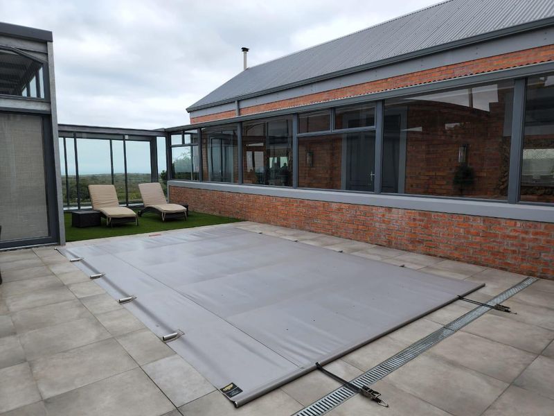 A well-maintained pool area featuring a covered swimming pool, paved surround, and a modern brick-clad building with large glass windows.