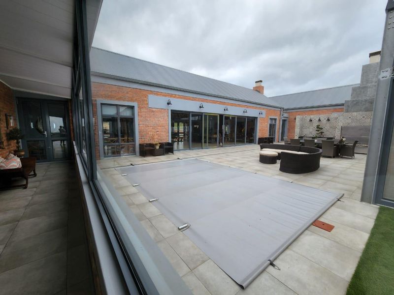 Spacious paved courtyard featuring a covered swimming pool, brick exterior walls, and large glass sliding doors leading into the main living area.