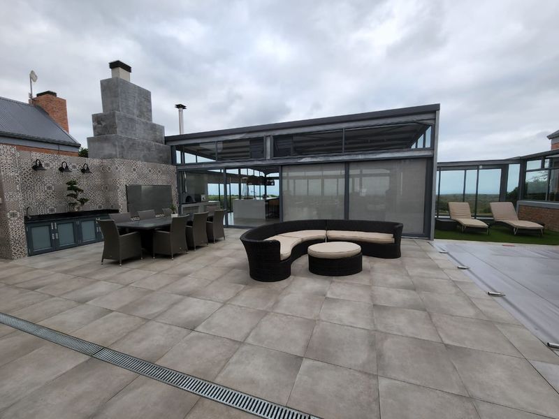 Spacious outdoor patio area featuring a built-in braai, decorative tiled backsplash, large format floor tiles, and seamless integration with the indoor living space.