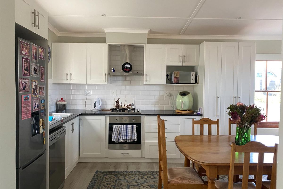 A bright, modern kitchen featuring white cabinetry, subway tile backsplash, dark countertops, built-in oven, gas hob, and an integrated extractor fan.