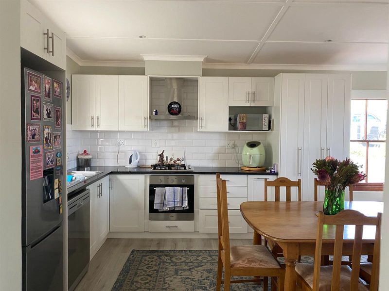 A bright, modern kitchen featuring white cabinetry, subway tile backsplash, dark countertops, built-in oven, gas hob, and an integrated extractor fan.