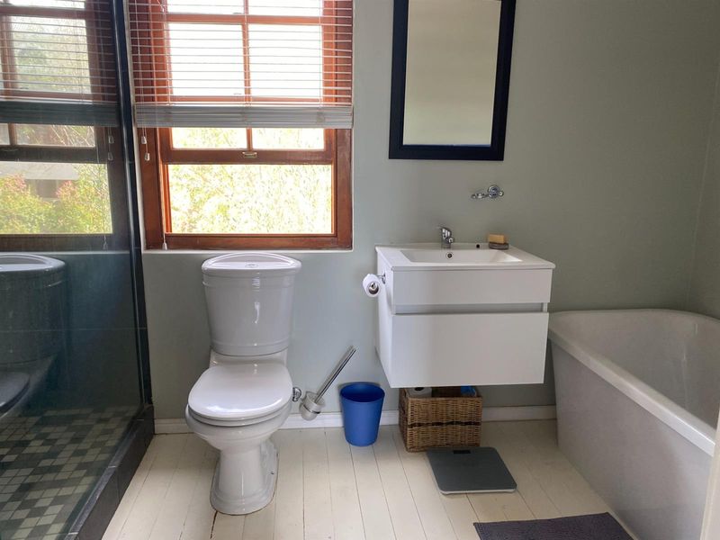 A functional bathroom featuring a wall-mounted vanity, a white toilet, a bathtub, and a separate shower enclosure with a wooden-framed window.