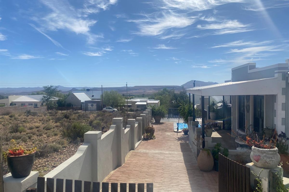 A view of the property exterior featuring a brick-paved walkway, a covered patio area, and a swimming pool overlooking the surrounding landscape.