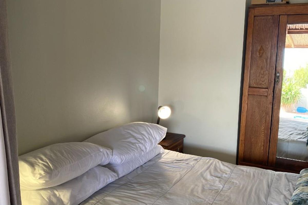 A cozy bedroom featuring neutral wall tones, a ceiling fan, and a built-in wooden wardrobe with a mirrored door.