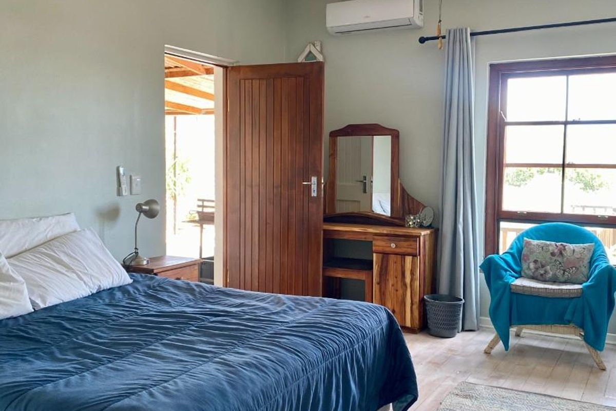 A bedroom featuring a ceiling fan, wall-mounted air conditioning unit, timber door, and window with natural light, providing access to an outdoor area.