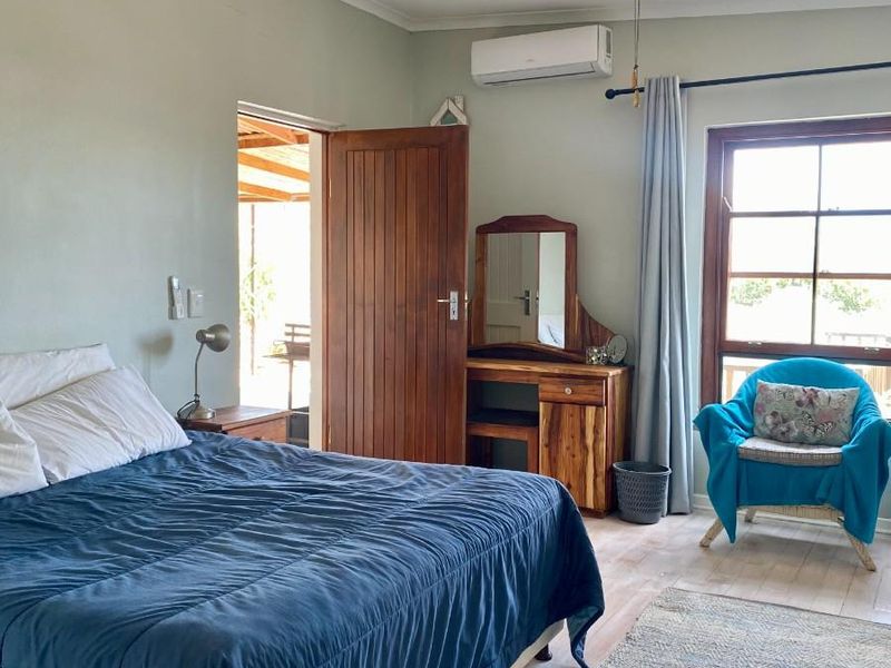 A bedroom featuring a ceiling fan, wall-mounted air conditioning unit, timber door, and window with natural light, providing access to an outdoor area.