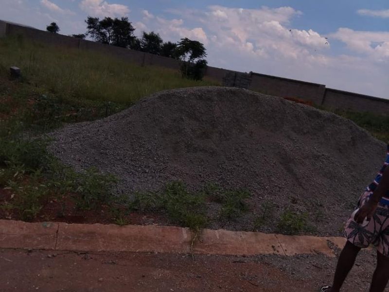 A view of a vacant residential plot featuring a perimeter wall and a pile of gravel on the site.