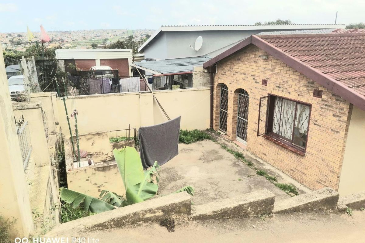 Rear exterior view of a brick house featuring a paved courtyard area, perimeter boundary walls, and metal security gates on windows and doors.