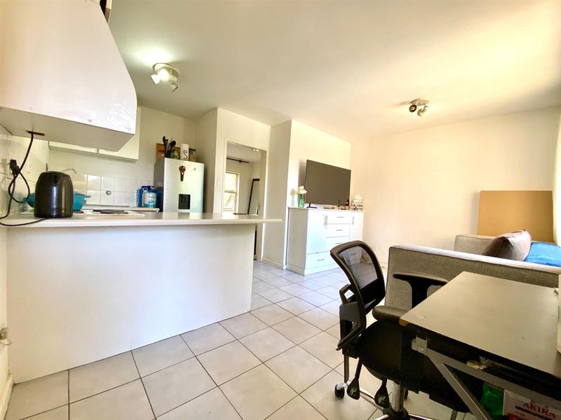 Open-plan living area featuring tiled flooring and a functional kitchen with a breakfast bar, providing a versatile space for cooking and relaxation.