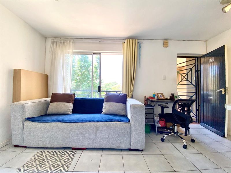 A living area featuring tiled flooring, a sliding glass door with natural light, and a security gate at the entrance.