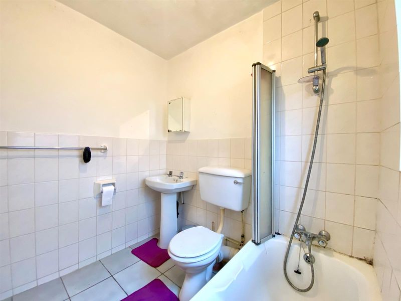 A functional bathroom featuring a pedestal sink, toilet, and a bathtub with a shower mixer and glass screen, finished with white wall tiles.