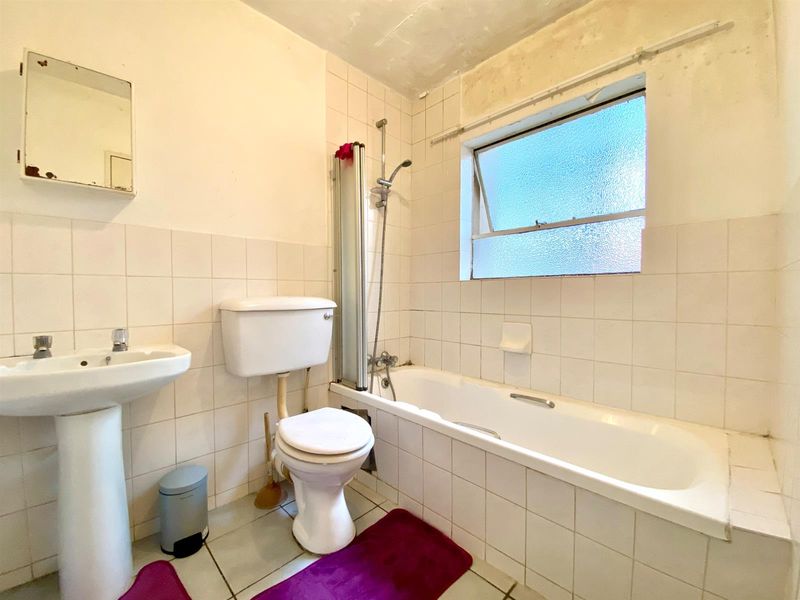 A dated bathroom featuring a pedestal basin, toilet, and bathtub with shower mixer, requiring cosmetic updates and repairs to wall and ceiling finishes.