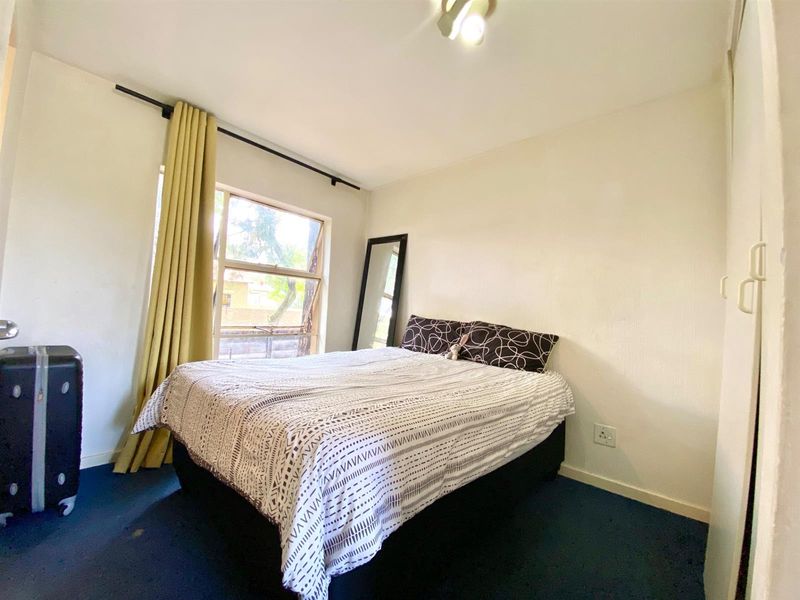 A functional bedroom featuring a built-in wardrobe, large window with curtain rod, and carpeted flooring.