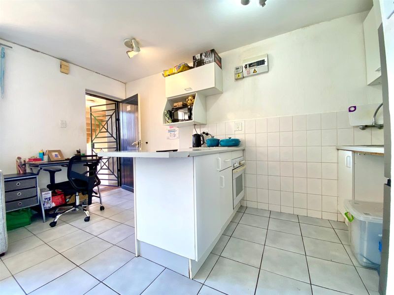 Compact kitchen featuring built-in cabinetry, tiled backsplash, and tiled flooring, with an integrated oven and direct access to a secure exterior entrance.