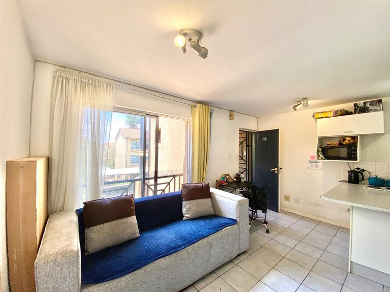 Open plan living area featuring tiled flooring, a sliding glass door leading to a balcony, and a compact kitchen with built-in cabinetry.
