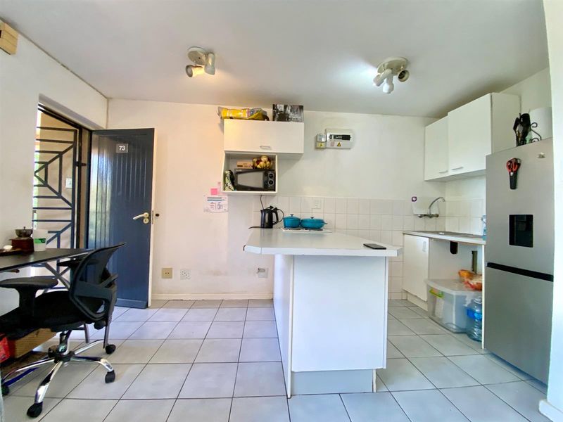 A functional kitchen area featuring tiled flooring, a central island, and white cabinetry, with direct access to an exterior security door.