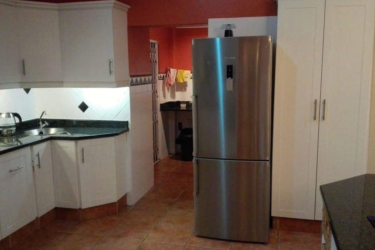 A functional kitchen featuring white cabinetry, dark granite countertops, and a tiled backsplash, with an adjacent scullery area visible in the background.