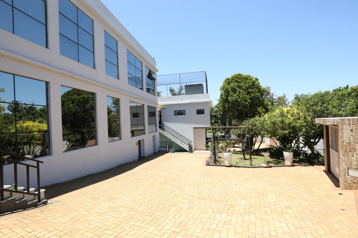 A spacious paved rear courtyard area featuring large glass windows, an external staircase, and landscaped garden elements.