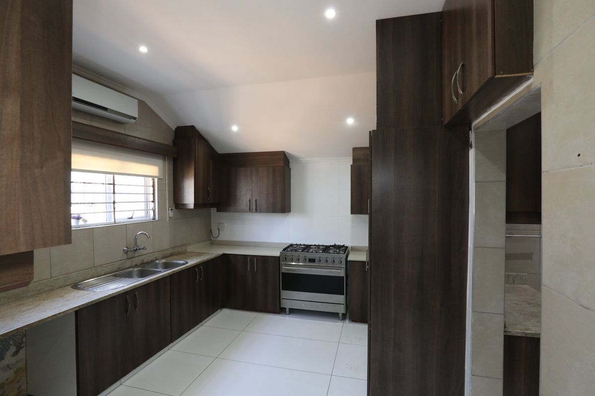 A modern kitchen featuring dark wood cabinetry, stone countertops, a stainless steel gas stove, and tiled flooring with recessed lighting.