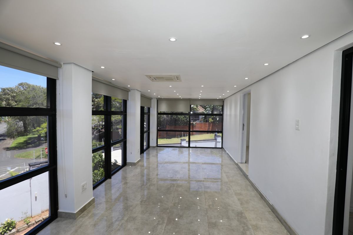 A bright, modern, and empty living area featuring large format tiled flooring, recessed downlighting, ducted air conditioning, and expansive black-framed windows.