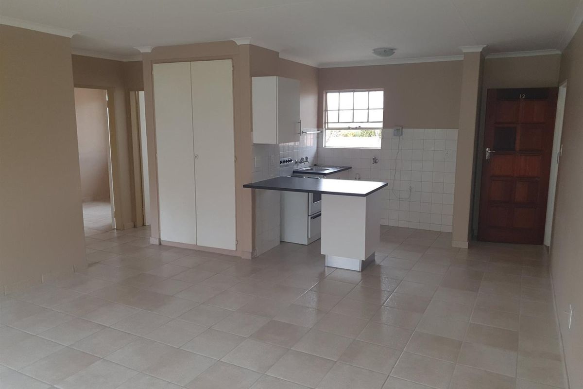 An open-plan kitchen and living area featuring tiled flooring, built-in cabinetry, and a functional layout with direct access to the entrance.