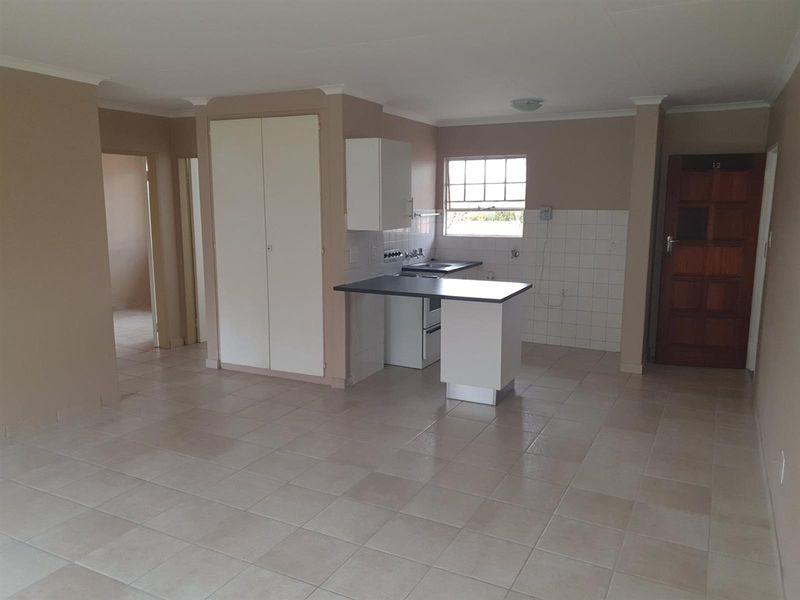 An open-plan kitchen and living area featuring tiled flooring, built-in cabinetry, and a functional layout with direct access to the entrance.