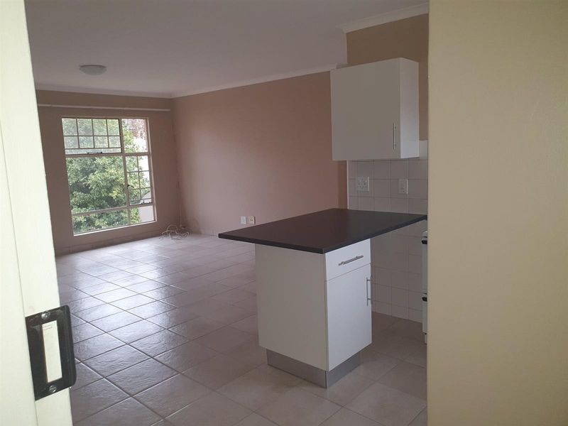 An open-plan living and kitchen area featuring tiled flooring, a breakfast counter, and large windows providing natural light.