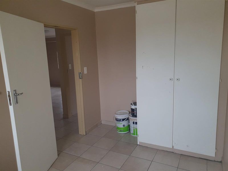 A bedroom featuring tiled flooring and built-in wardrobe storage, with a doorway leading to an adjacent living area.
