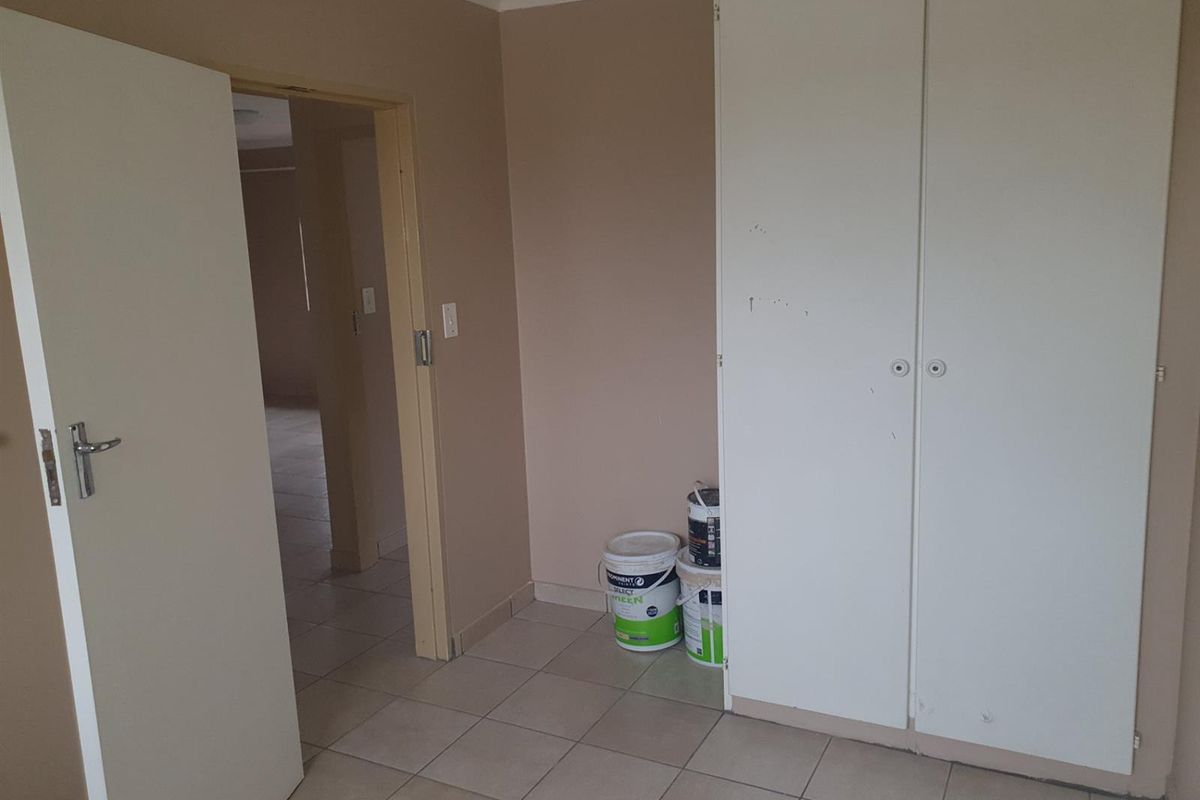 A bedroom featuring tiled flooring and built-in wardrobe storage, with a doorway leading to an adjacent living area.