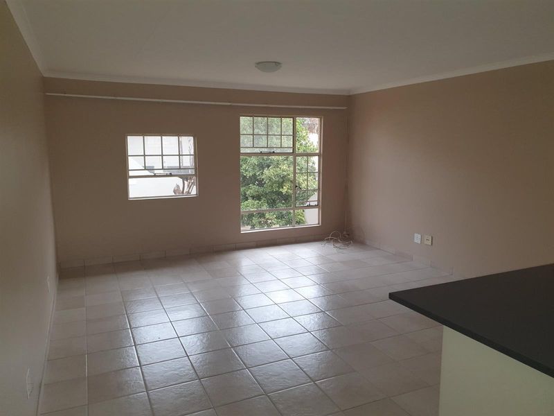 An empty, open-plan living area featuring neutral wall tones, tiled flooring, and large windows providing natural light.