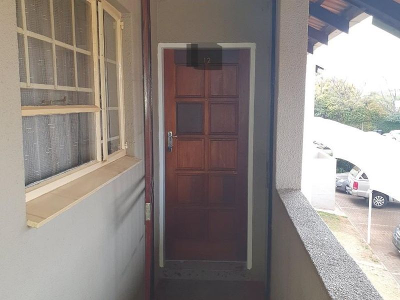 A covered townhouse entrance featuring a timber panelled front door, tiled flooring, and a security gate frame.
