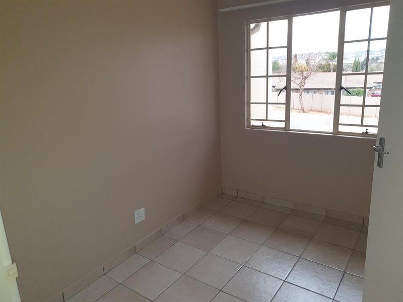 A compact, empty bedroom featuring neutral wall tones, tiled flooring, and a large window providing natural light and a view of the neighborhood.
