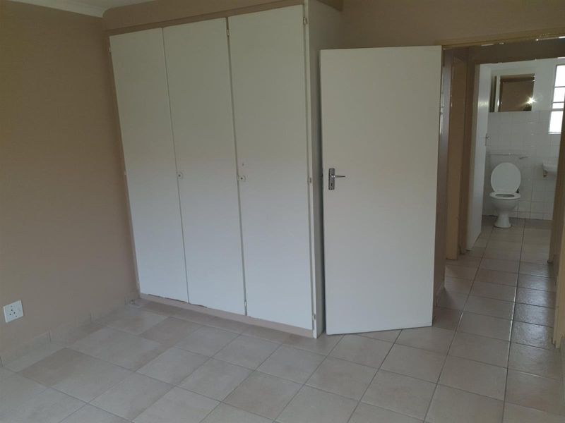 A bedroom featuring built-in cupboards and tiled flooring, with an adjacent view into a bathroom area.