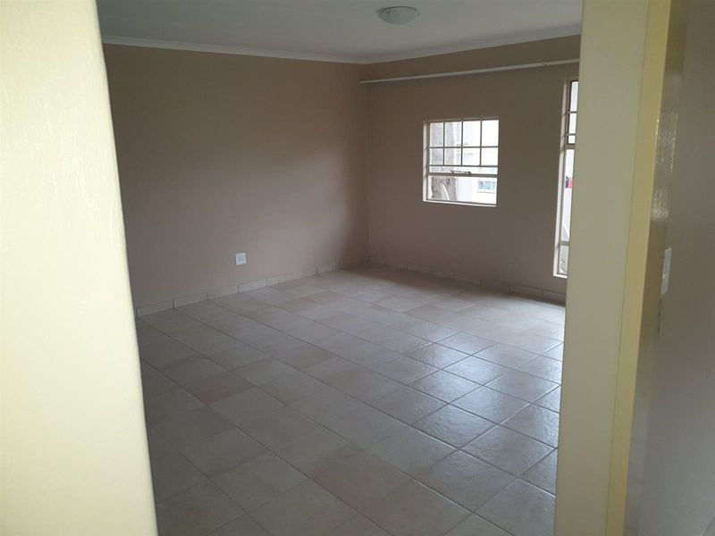 An empty, neutrally painted room featuring tiled flooring and large windows, providing a versatile space suitable for a bedroom or living area.