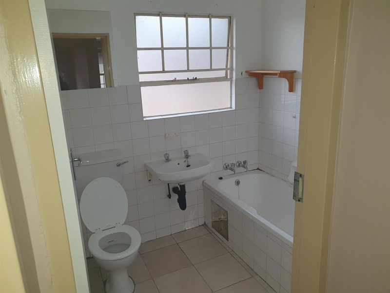 A dated bathroom featuring a standard bathtub, wall-mounted basin, and toilet with white wall tiling and tiled flooring.