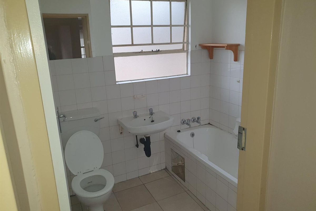 A dated bathroom featuring a standard bathtub, wall-mounted basin, and toilet with white wall tiling and tiled flooring.
