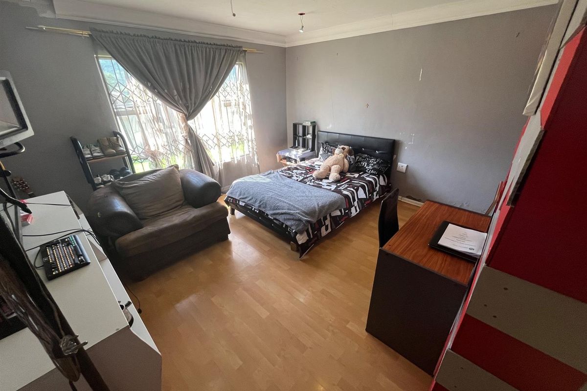 A standard bedroom featuring laminate flooring, recessed lighting, and a security gate on the window. The room requires minor cosmetic updates to the walls.