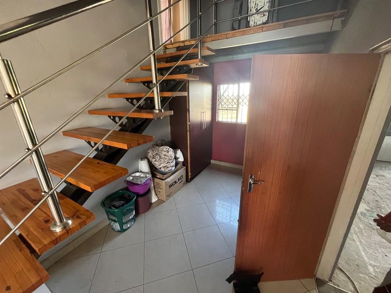 A hallway area featuring an open-tread timber staircase with stainless steel balustrades, tiled flooring, and a built-in storage cupboard.