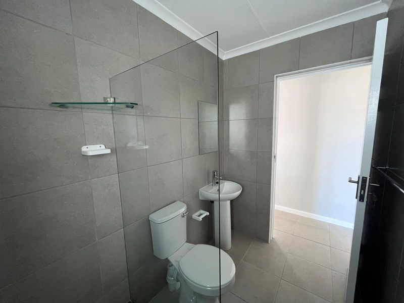 Modern bathroom featuring grey wall tiles, a glass shower screen, a pedestal basin, and a white toilet.