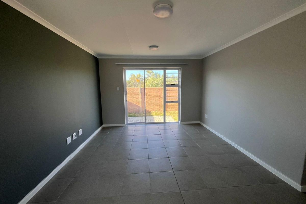 A bright, empty living room featuring neutral tiled flooring, a dark accent wall, and sliding glass doors providing access to the rear garden.