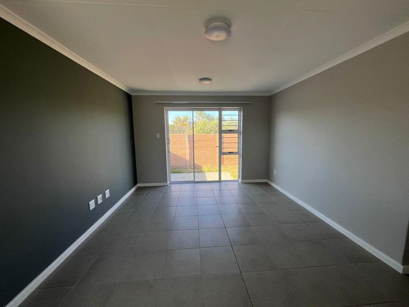 A bright, empty living room featuring neutral tiled flooring, a dark accent wall, and sliding glass doors providing access to the rear garden.