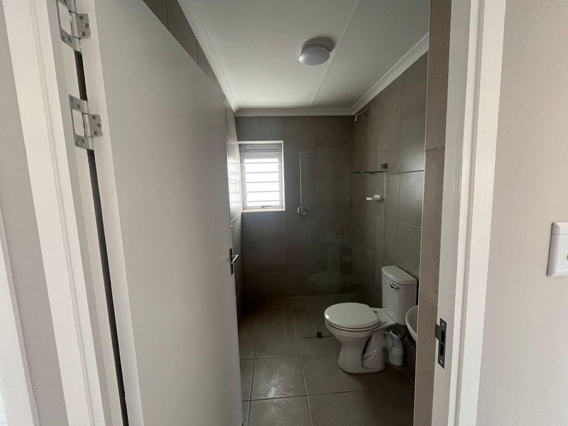 A compact bathroom featuring neutral floor-to-ceiling wall tiles, a walk-in shower enclosure, a standard toilet, and a small basin.